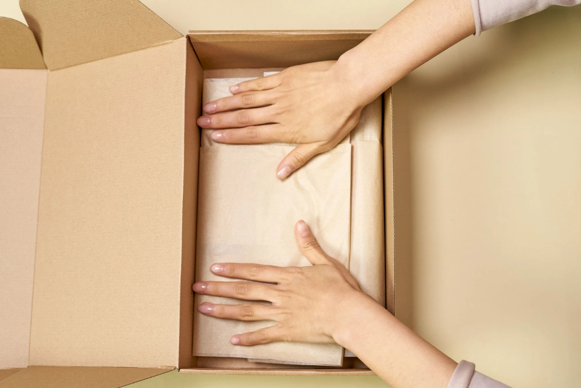 Hands arranging protective tissue paper inside an unbranded cardboard box