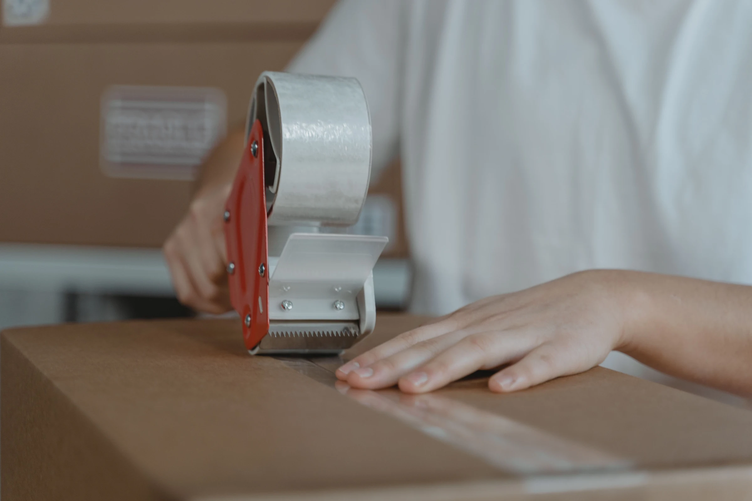 Hands sealing a cardboard carton with a tape dispenser before dispatch