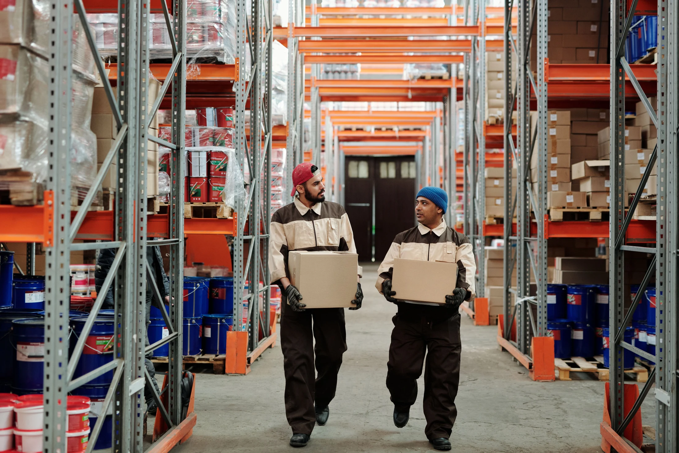 Warehouse workers carrying cartons between storage racks