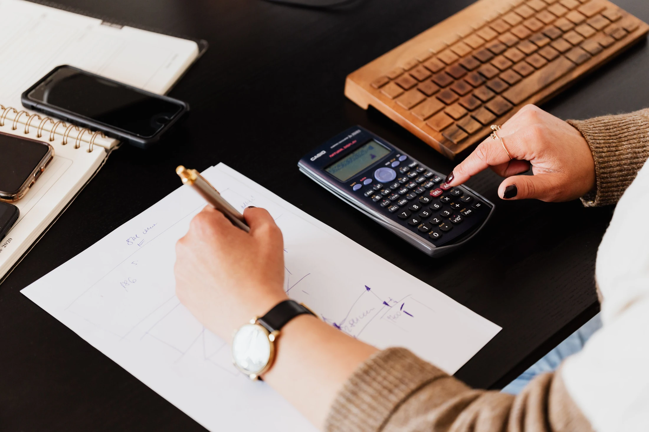 Hands using a calculator and making written cost calculations