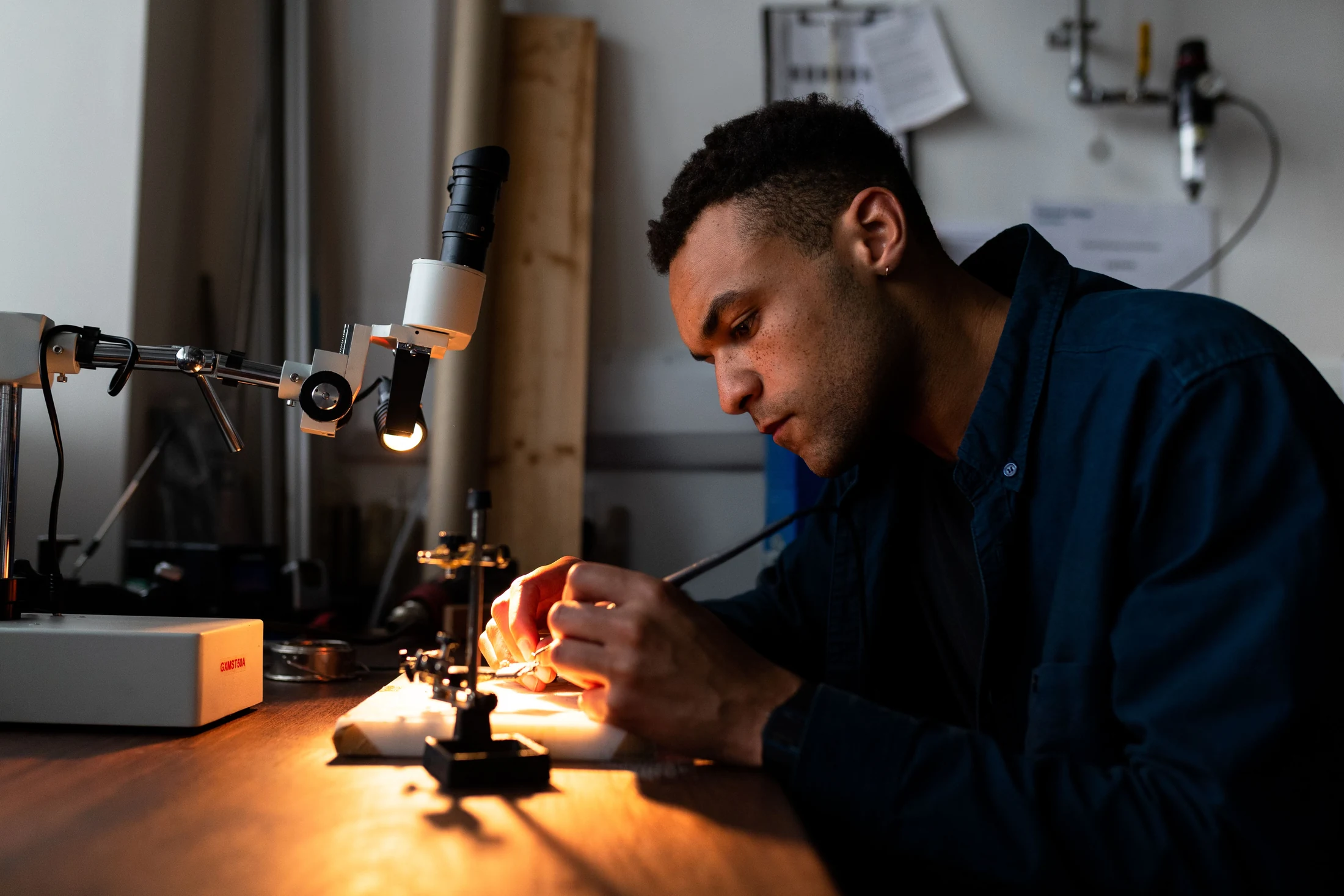 Engineer soldering electronic components at a workshop bench under a precision work light