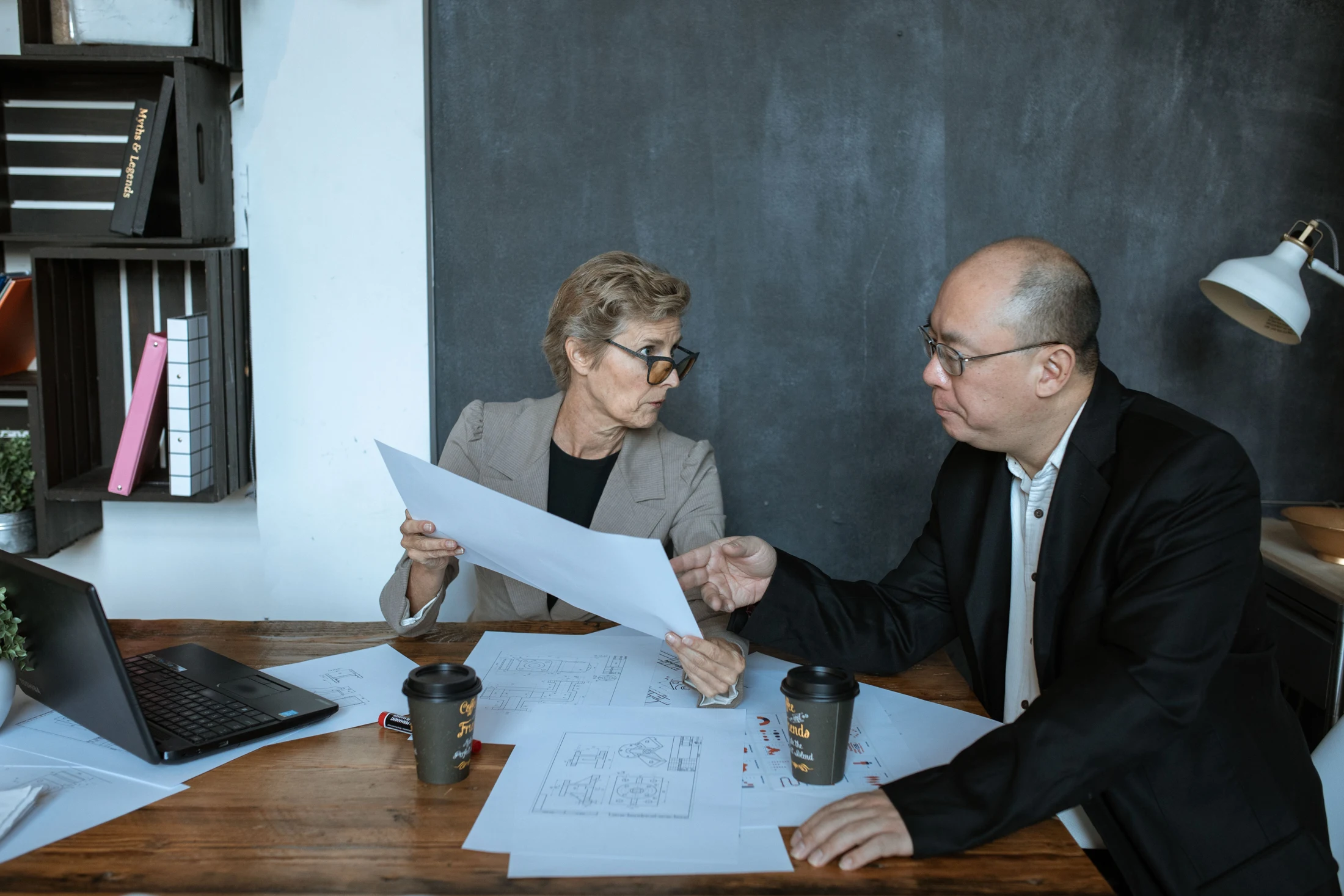 Two professionals reviewing project drawings and discussing requirements at a desk
