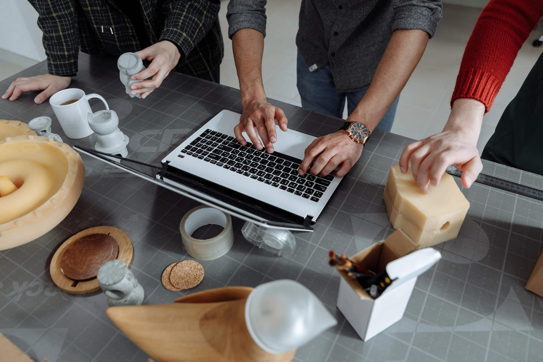 Three collaborators reviewing product samples and prototype components around a laptop