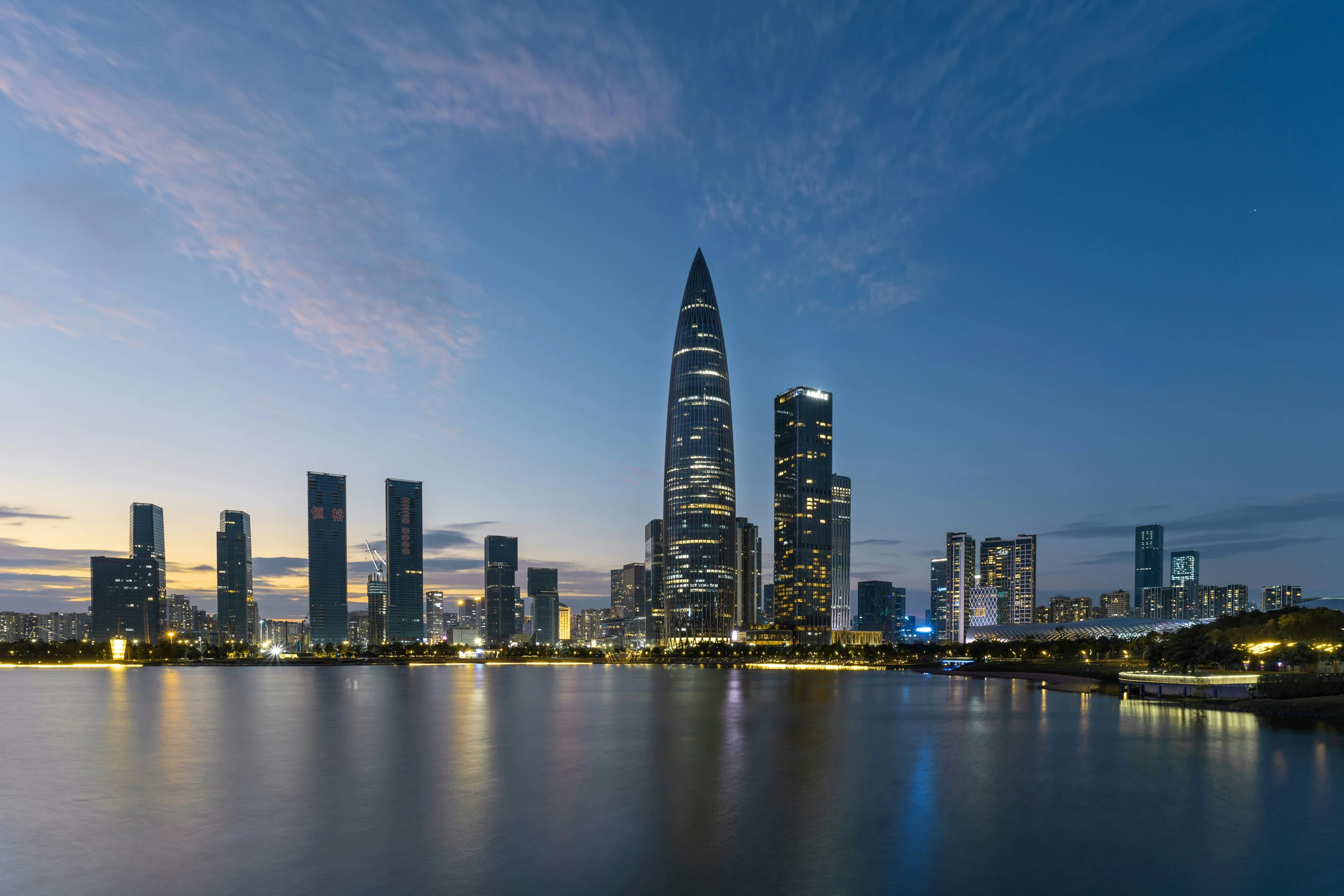 The illuminated Spring Bamboo tower and Houhai skyline across Shenzhen Bay at blue hour.