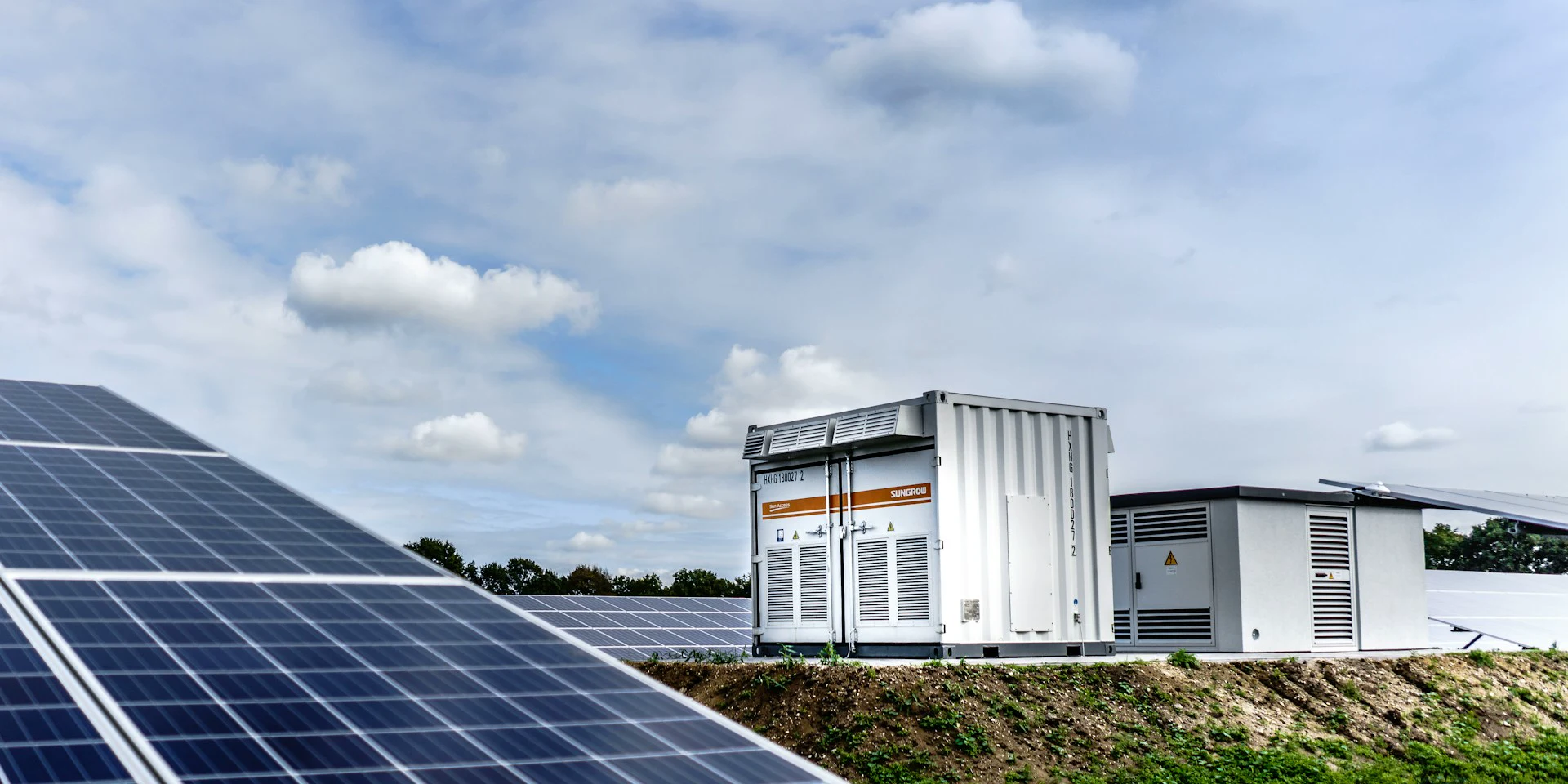 Foreground photovoltaic panels with central inverter equipment behind, viewed at an angle